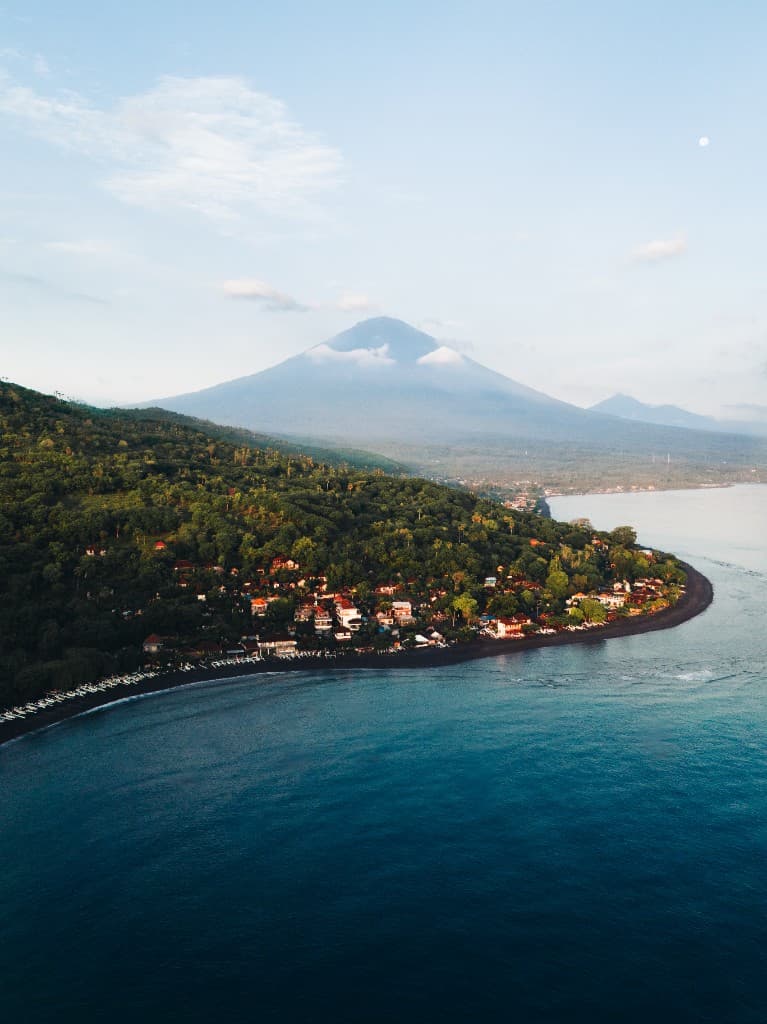 Aerial view of a volcanic coastline with a village and a towering mountain behind it.