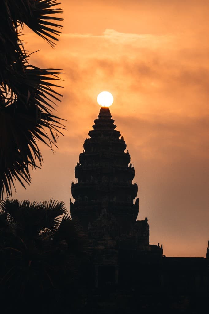 The sun resting on the central spire of Angkor Wat at sunset.