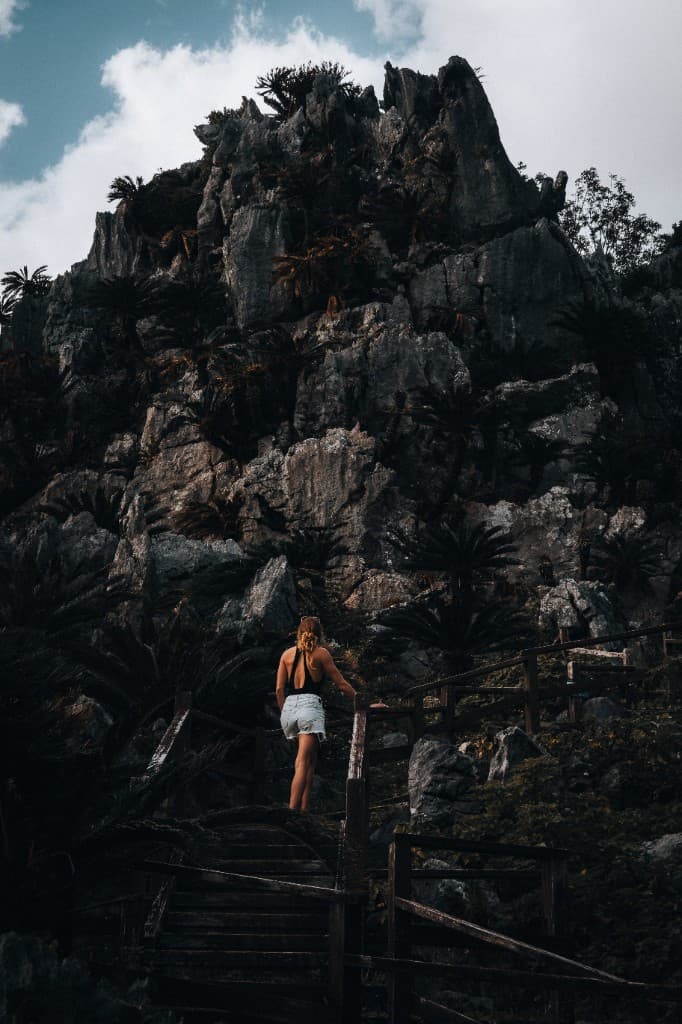 A person climbing weathered wooden stairs toward a massive limestone cliff.