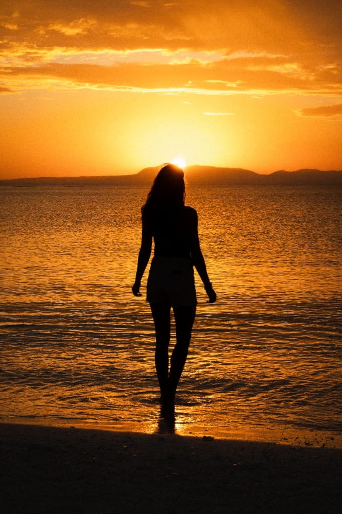 A silhouetted figure standing in calm golden water at sunset.