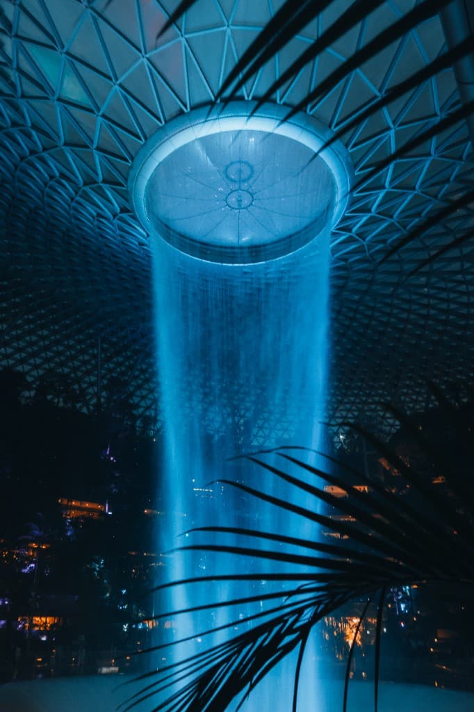 A towering indoor waterfall lit in blue beneath a geometric glass dome.