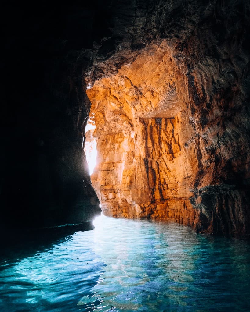 Turquoise water inside a sunlit sea cave with golden rock walls.
