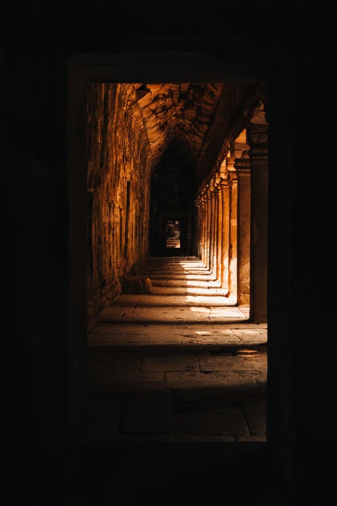 Golden light illuminating a stone temple corridor disappearing into shadow.