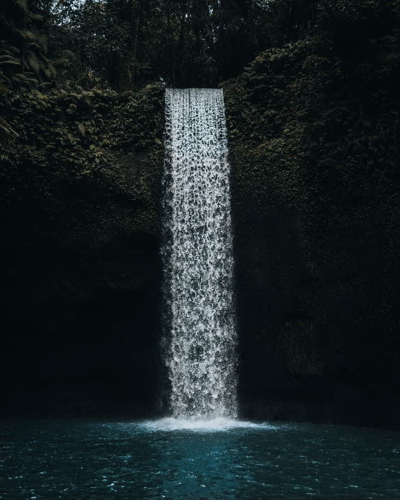 A waterfall cascading into a dark teal pool surrounded by moss-covered walls.